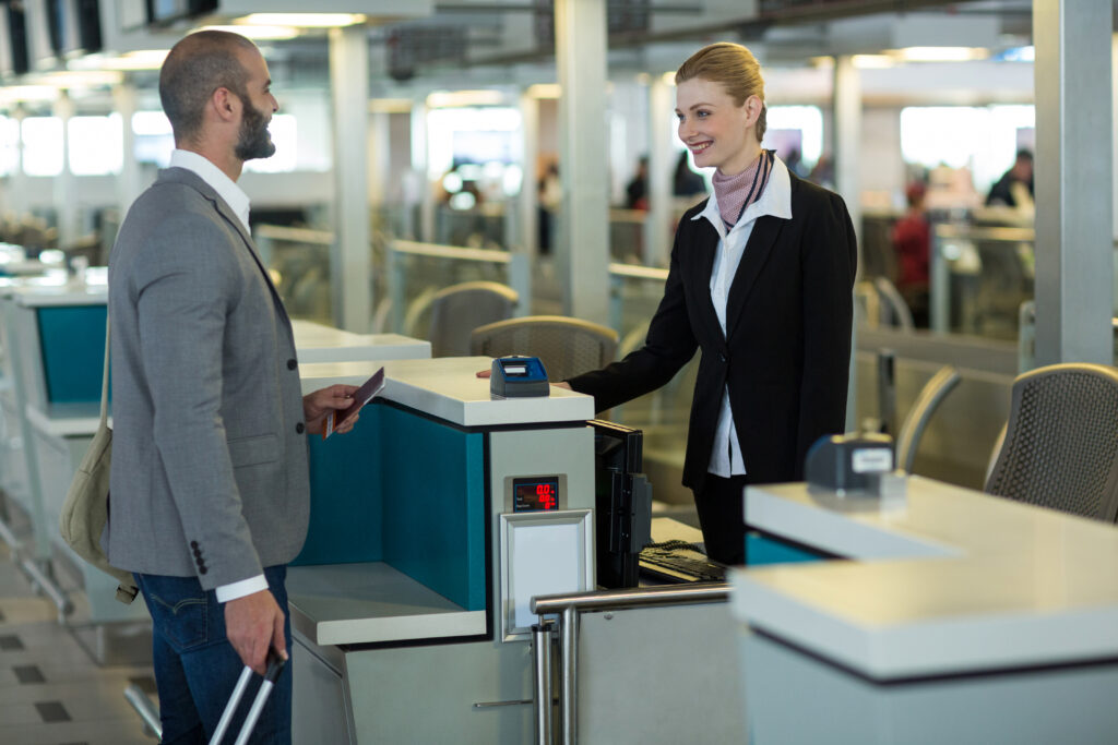 Passageiro interage com atendente no balcão de check-in do aeroporto, apresentando passaporte.