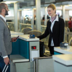 Passageiro interage com atendente no balcão de check-in do aeroporto, apresentando passaporte.