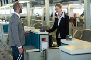 Passageiro interage com atendente no balcão de check-in do aeroporto, apresentando passaporte.