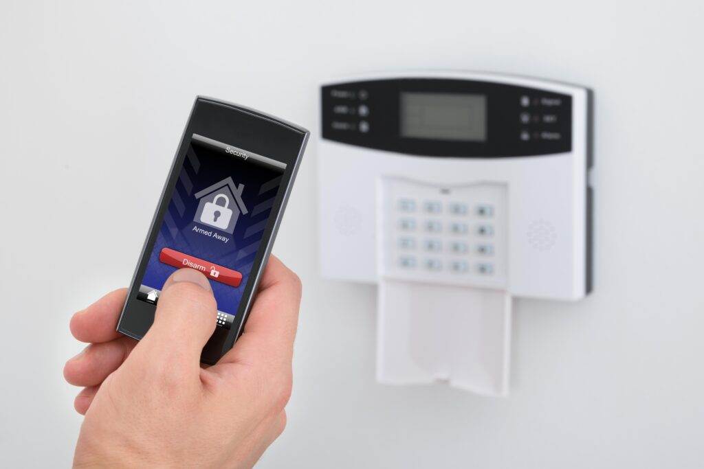 Pessoa usando um celular para desarmar um sistema de segurança residencial, com um painel de controle ao fundo.