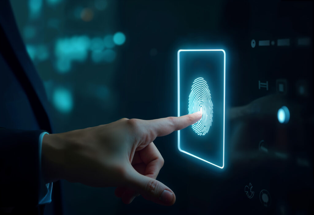 Mão de uma pessoa tocando uma tela digital iluminada em azul, que exibe uma impressão digital. A cena sugere autenticação biométrica por impressão digital em um painel tecnológico.