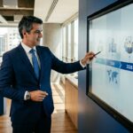 Executivo em traje formal aponta para tela interativa exibindo o roadmap estratégico de expansão e segurança digital para os anos de 2024 a 2027.